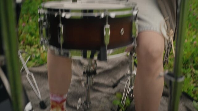 Caucasian young woman playing drum kit outdoors in field with camera tilting up. Footage suitable for youth lifestyle commercials, indie music videos, and festival promotions