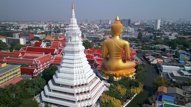 Aerial drone view of giant golden Buddha at Wat Paknam temple with Bangkok skyline in the background. Iconic religious landmark in Thailand.