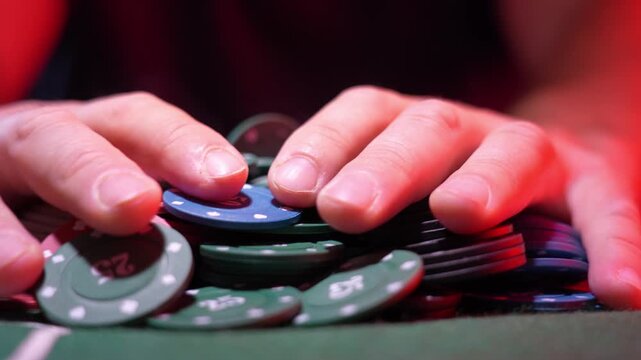 Close-up of green poker table. Poker chips scattered on surface. Red jacket blurred in background. Hand moves toward chips. Intense gambling moment. Ideal for casino or poker projects