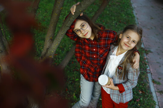 Two Happy Girls in Stylish Outfits Smiling Outdoors Near Tree