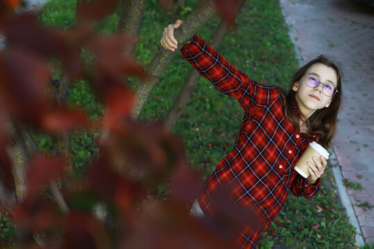 Young Girl in Red Plaid Shirt Enjoying Autumn with Coffee in Park