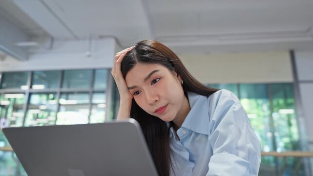 Tired Asian office worker resting her head on her hand while looking at a laptop screen, struggling to adapt to new AI tools and changing workplace skill demands.