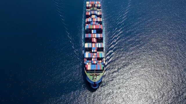 High aerial view of a large container cargo vessel traveling over sparkling ocean