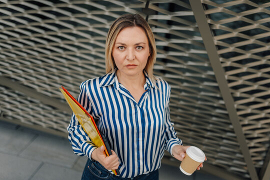 Professional woman carrying folders and coffee cup