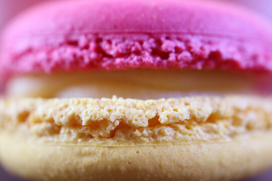 Extreme macro texture of a pink raspberry macaron with creamy filling, focusing on the intricate macaron feet