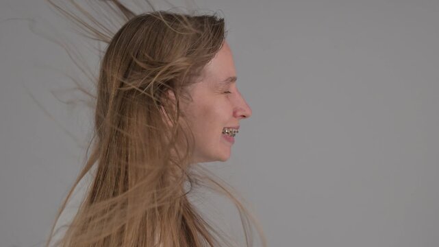 A portrait of a Caucasian woman with braces. A sudden gust of air flutters her hair.