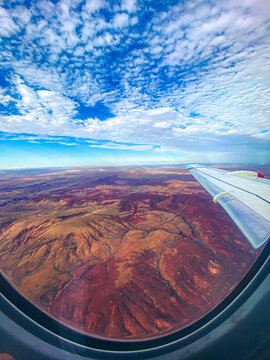 Airplane wing flying over red desert landscape under blue sky