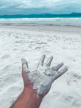 Hand holding white sand at a tropical beach