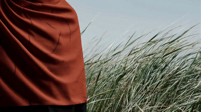Textured reddish-orange scarf wrapped tightly while standing still outdoors beside tall green grass