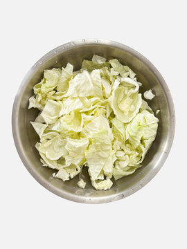 Top view of chopped fresh green cabbage leaves washed in a stainless steel bowl, isolated on a white background. Essential ingredient for healthy cooking and food preparation.