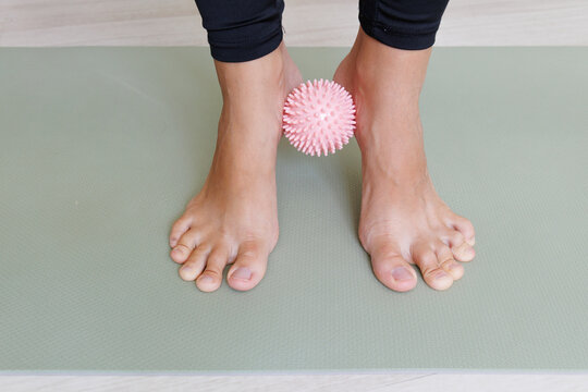 Preventive foot exercise squeezes a massage ball between the ankles to train alignment, arch control, balance and lower leg muscles, supporting flat feet and ankle instability prevention.
