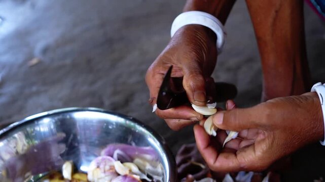 Woman peeling and cleaning fresh garlic cloves with a small knife in a rural village kitchen.