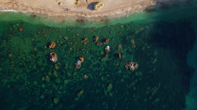Aerial view of rocky shoreline and clear shallow water along a sandy beach at sunset