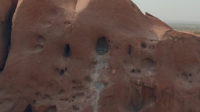 Drone close-up of a weathered rock wall in the Thar Desert, Sindh, Pakistan, revealing a bird nest inside a deep cavity among eroded hollows and vertical fissures.