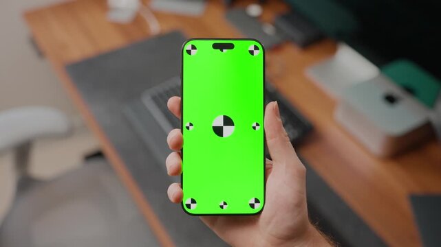 Person rotates smartphone with green screen tracking marks in a modern office setting