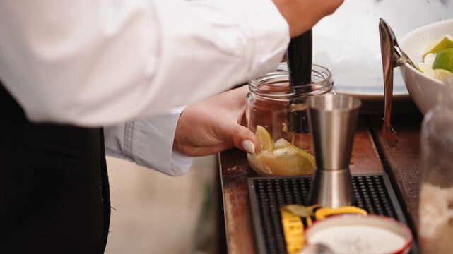 Bartender hands muddling fresh lime and sugar in a glass for preparing a refreshing caipirinha or mojito drink