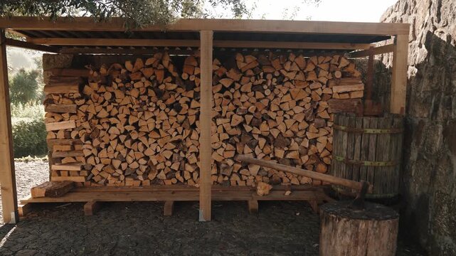 Firewood stacked in a sturdy wooden shelter next to a rustic stone wall, prepared for winter and sustainable energy
