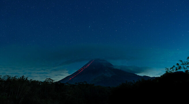 Mount merapi volcano erupting lava under starry night sky