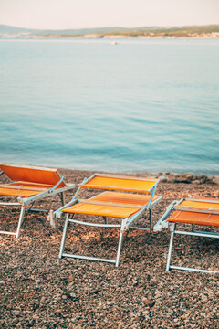Empty orange beach loungers on a pebble shore in Kvarner Bay, Croatia. Concept of Mediterranean summer vacations and seaside relaxation.