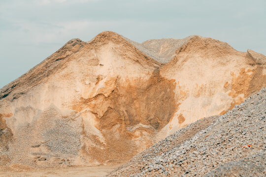 Industrial stockpiles of gravel and crushed rock forming textured mounds against a pale blue sky. Construction materials, aggregate production, quarry industry and infrastructure concept.