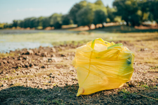 Yellow trash bag full of collected plastic pollution on a riverbank. Concept of environmental cleanup initiatives, volunteer waste collection, water protection, and eco-restoration.