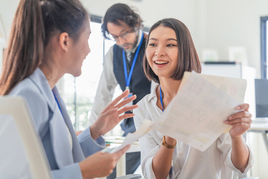 Cheerful Asian businesswomen sharing creative paperwork during brainstorming session in modern office, demonstrating positive collaboration, enthusiastic feedback, strategic teamwork, and startup syne