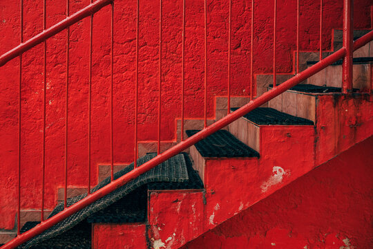 Side view of outdoor staircase steps with black rubber treads against a bright red textured wall and railing.