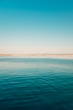 Minimalist seascape view of calm blue water under a clear gradient blue sky with distant coastline horizon.