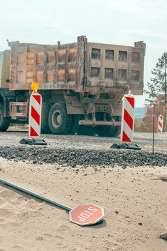 Overturned stop sign in front of a heavy construction truck at a roadwork site. Concept of infrastructure development, civil engineering, traffic hazards, and work zone safety.