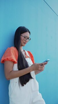 Young asian woman smiling while using smartphone outdoors