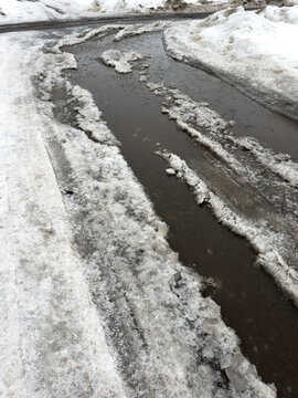 Snowy roadside with melting water flowing through icy channels
