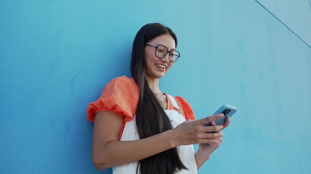 Young asian woman using a smartphone against a blue background