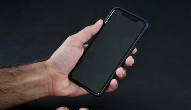 Hand holding a black smartphone against a dark background, 4K video