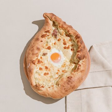Khachapuri adjaruli with melted cheese and a runny egg yolk on a clay surface, rustic and warm for hospitality marketing and breakfast