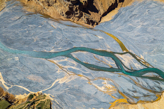 Aerial view of a braided river flowing through the gravel canyon floor, creating abstract natural patterns in Anjihai Grand Canyon, Xinjiang, China