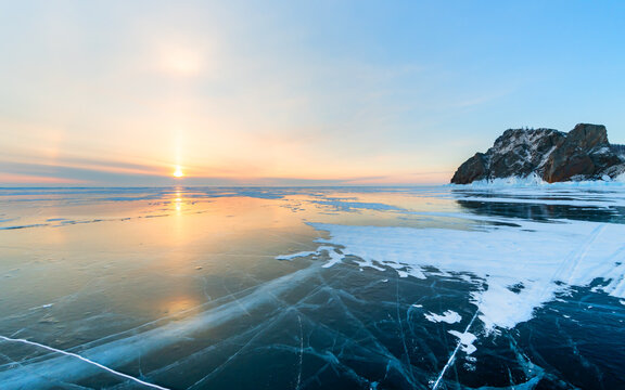 Blue transparent cracked ice on Baikal lake in winter. Khoboy cape of Olkhon island, Baikal, Russia. Winter landscape at sunrise.
