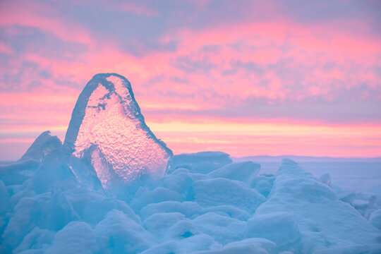 Blue transparent ice on Baikal lake at sunrise. Pink sky with clouds in the blurred background. Baikal, Siberia, Russia