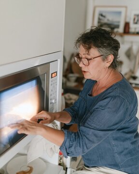 Senior Latina woman adjusting a glowing oven clock in a dark kitchen, natural scene of turning back the clock for appliance campaigns