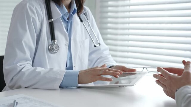 Doctor consulting patient, discussing medical information and diagnosis using a digital tablet during a healthcare visit at a modern clinic office