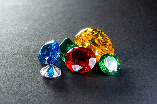 Colorful faceted gems in blue, red, green, and yellow arranged on a dark surface, showcasing brilliance, sparkle, luxury, jewelry design, gemstone beauty, and elegant still life photography