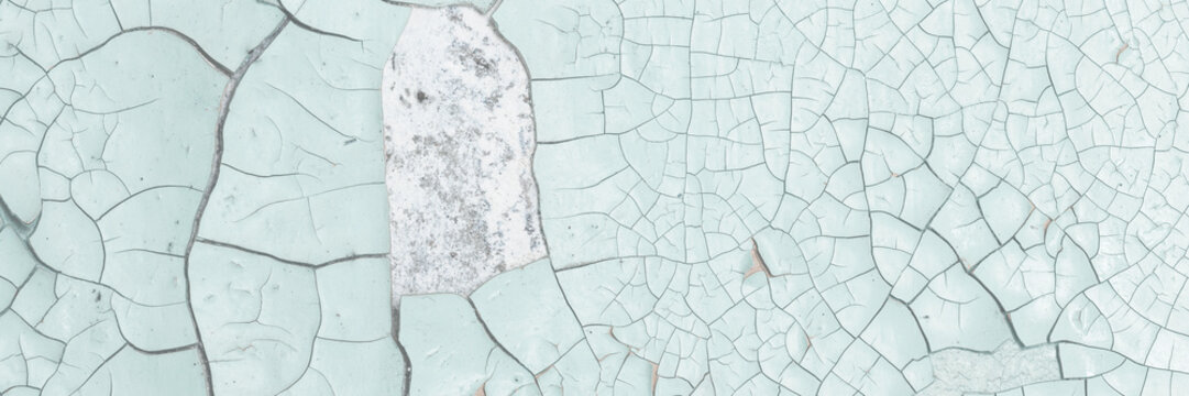 Green peeling paint on the wall. Old concrete wall with cracked flaking paint. Weathered rough painted surface with patterns of cracks and peeling. High resolution texture for background and design.