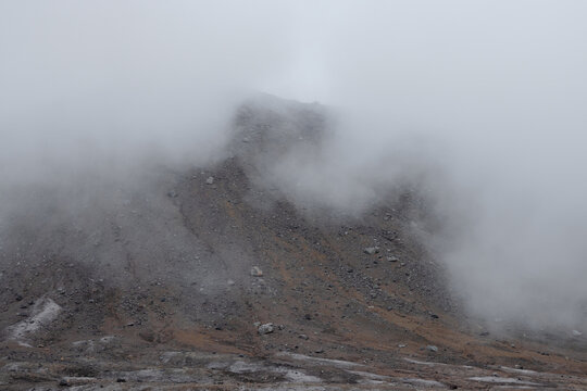 Foggy mountain landscape. View of the top of the volcano in the clouds. Low clouds and poor visibility. Travel, tourism and hiking on the Kamchatka Peninsula. Gorely volcano, Kamchatka Krai, Russia.
