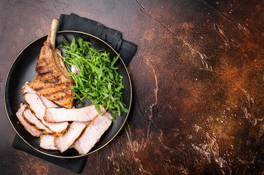 Succulent grilled Tomahawk pork chop, rib bone in steak featuring crispy edges and juicy meat that will tantalize your taste buds. brown background. top view