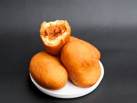 Luti gendang sit on a white plate. One is bitten, revealing a savory filling. Dark background highlights the food's rich color. Appealing to food lovers and casual eaters