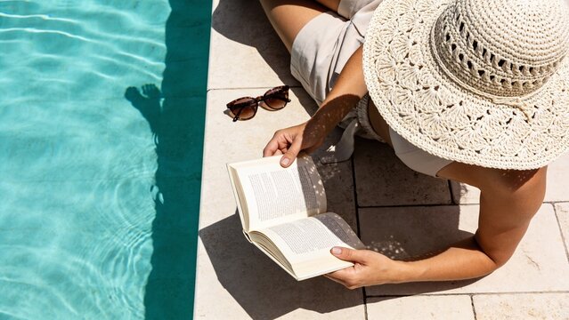 Relaxed Woman Reading Book Beside Turquoise Swimming Pool on Sunny Resort Terrace