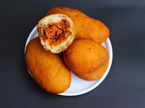 Luti gendang sit on a white plate. One is bitten, revealing a savory filling. Dark background highlights the food's rich color. Appealing to food lovers and casual eaters