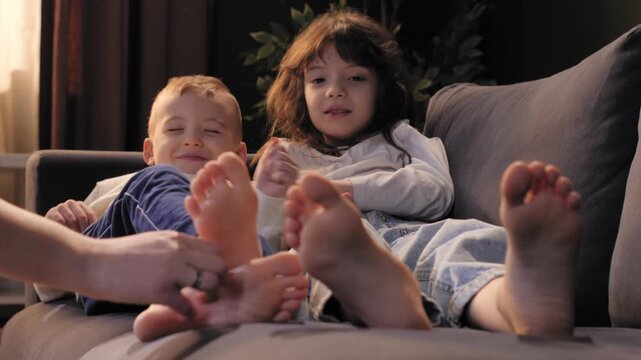 Mother tickling feet of daughter and son on sofa