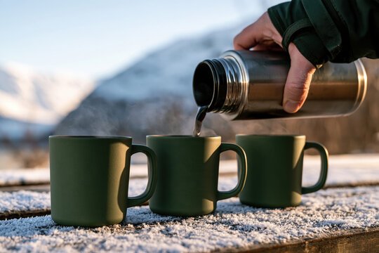 Pouring hot coffee into mugs during winter mountain trip