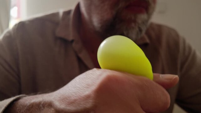 Close-up of man continually squeezing a soft yellow ball, evoking workplace stress, concentration, relaxation and tactile coping behaviour.