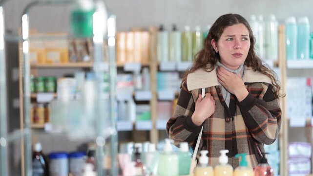 Young woman buyer with sore throat choosing medicines and hygiene products in pharmacy 